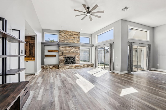 unfurnished living room featuring ceiling fan, a fireplace, light hardwood / wood-style flooring, and a high ceiling