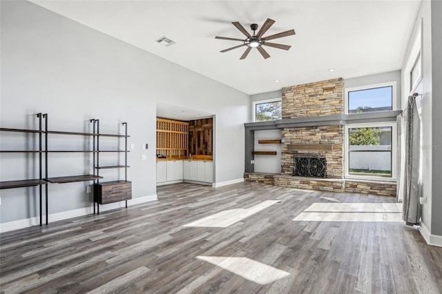 unfurnished living room with hardwood / wood-style flooring, a stone fireplace, and ceiling fan