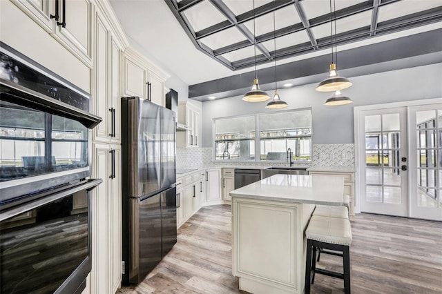 kitchen featuring a kitchen island, sink, stainless steel appliances, wall chimney range hood, and french doors