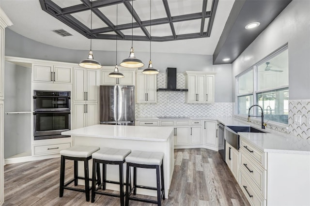 kitchen with a kitchen island, sink, backsplash, black appliances, and wall chimney range hood