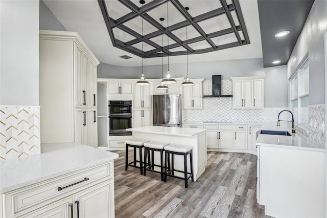 kitchen with sink, hanging light fixtures, stainless steel fridge, a kitchen breakfast bar, and wall chimney range hood