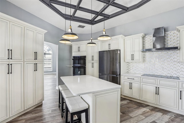 kitchen featuring a center island, tasteful backsplash, coffered ceiling, black appliances, and wall chimney exhaust hood