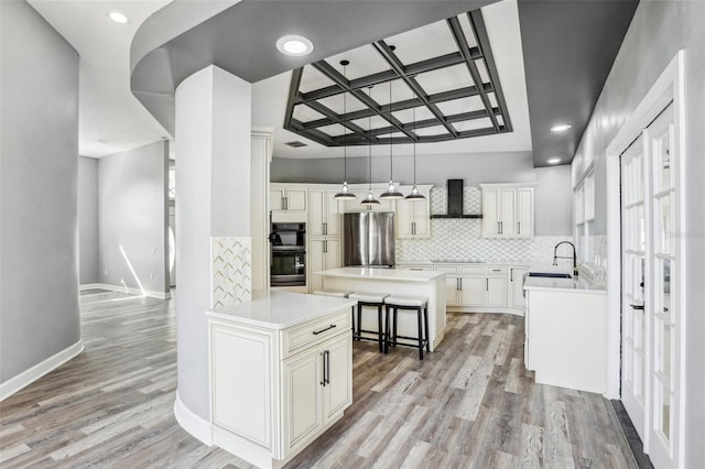 kitchen with pendant lighting, wall chimney range hood, stainless steel fridge, white cabinetry, and a center island