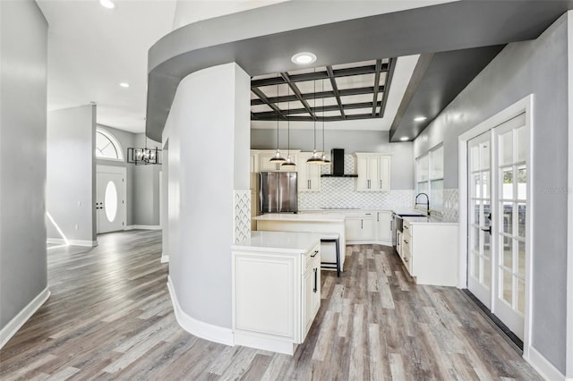 kitchen featuring sink, stainless steel refrigerator, hanging light fixtures, white cabinets, and wall chimney exhaust hood