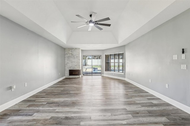 unfurnished living room with ceiling fan, wood-type flooring, a stone fireplace, and a tray ceiling