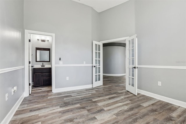 unfurnished bedroom featuring french doors, connected bathroom, sink, and light hardwood / wood-style flooring