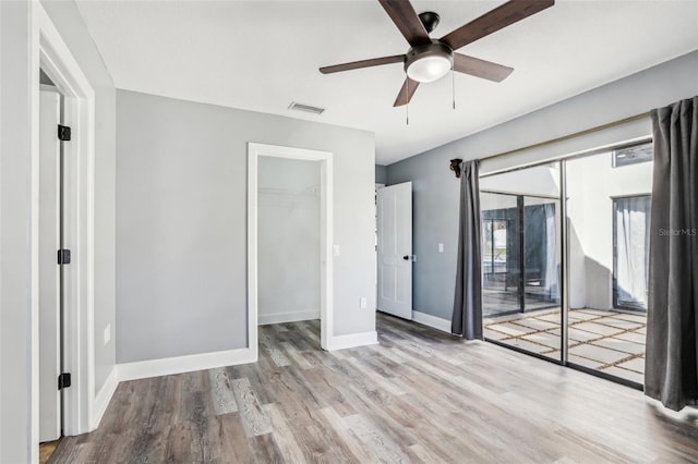 unfurnished bedroom with ceiling fan, a spacious closet, a closet, and light wood-type flooring