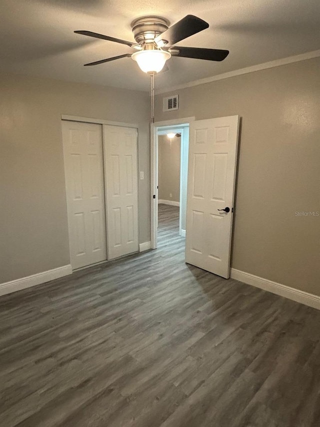 unfurnished bedroom with ornamental molding, dark wood-type flooring, ceiling fan, and a closet