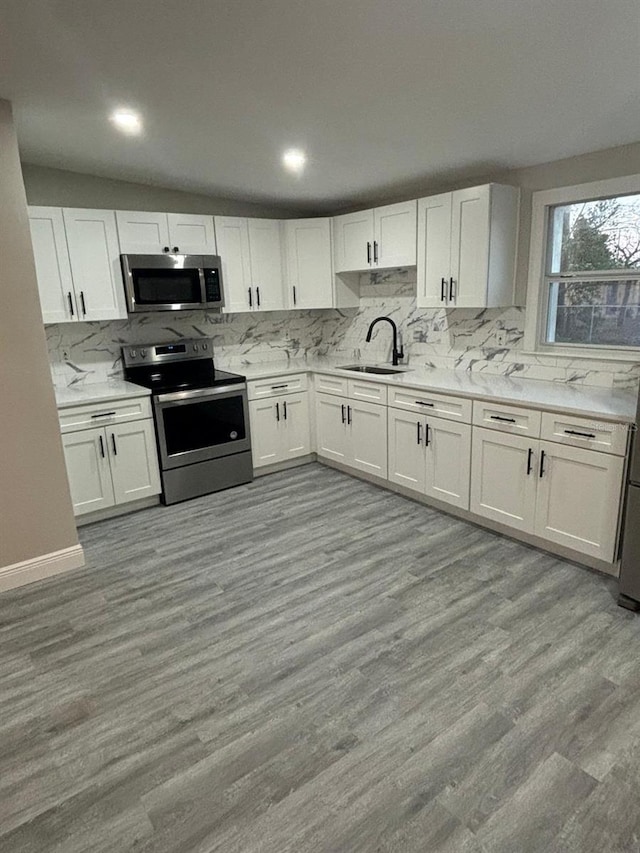 kitchen with white cabinetry, stainless steel appliances, sink, and light hardwood / wood-style flooring