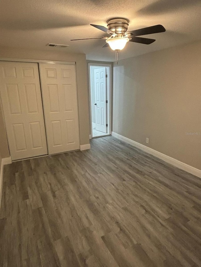 unfurnished bedroom with dark wood-type flooring, ceiling fan, a closet, and a textured ceiling