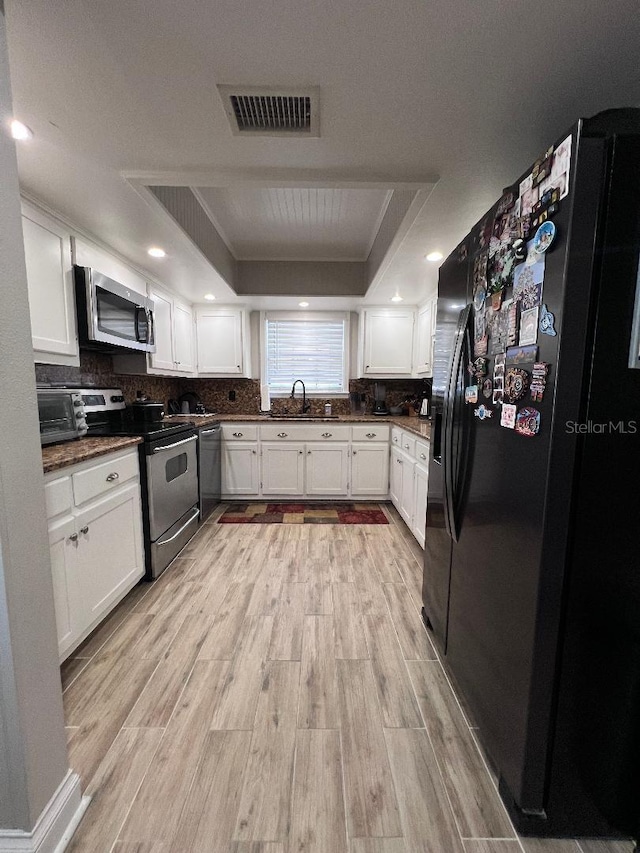 kitchen featuring appliances with stainless steel finishes, a raised ceiling, light hardwood / wood-style flooring, and white cabinets