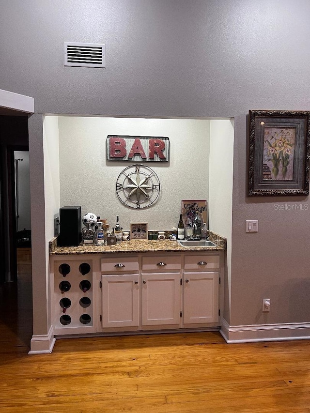 bar with light stone countertops, sink, and light hardwood / wood-style flooring