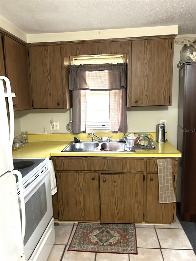 kitchen with white electric range oven, light countertops, light tile patterned flooring, a sink, and a textured ceiling