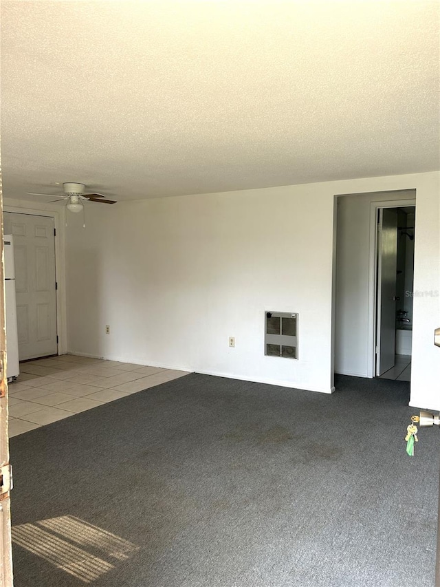 carpeted empty room featuring heating unit, a textured ceiling, a ceiling fan, and tile patterned floors