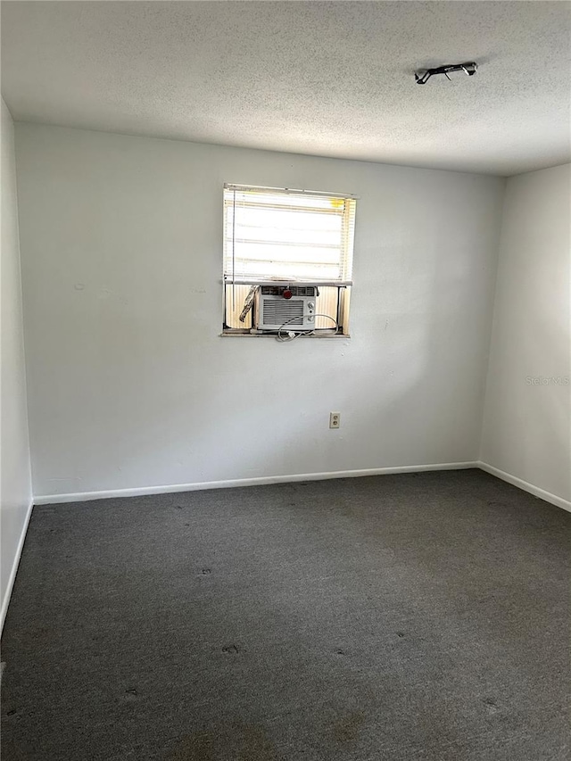 spare room with a textured ceiling, carpet, cooling unit, and baseboards