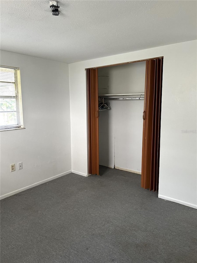 unfurnished bedroom featuring dark colored carpet, a closet, a textured ceiling, and baseboards