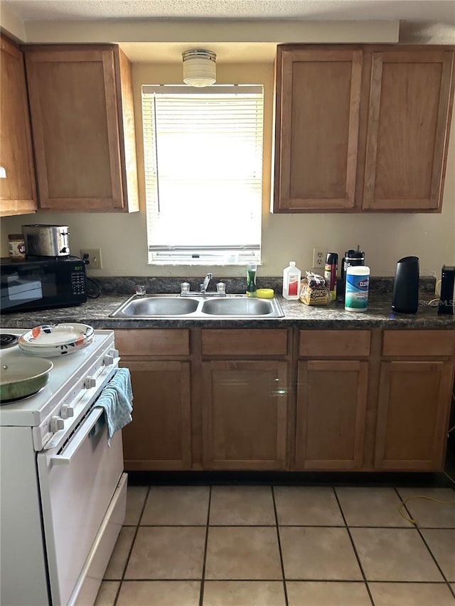 kitchen with light tile patterned floors, dark countertops, white stove, black microwave, and a sink