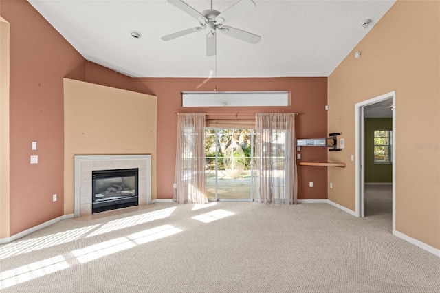 unfurnished living room featuring a tiled fireplace, plenty of natural light, light colored carpet, and ceiling fan