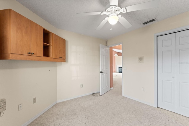 interior space with ceiling fan, light colored carpet, a closet, and a textured ceiling