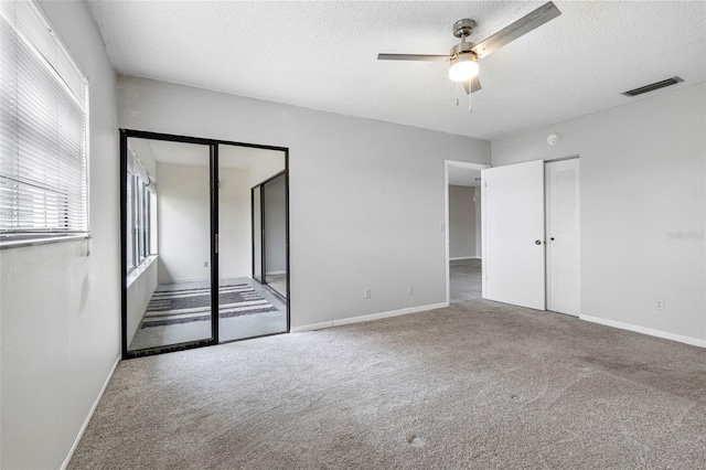 unfurnished bedroom featuring ceiling fan, carpet flooring, a textured ceiling, and two closets