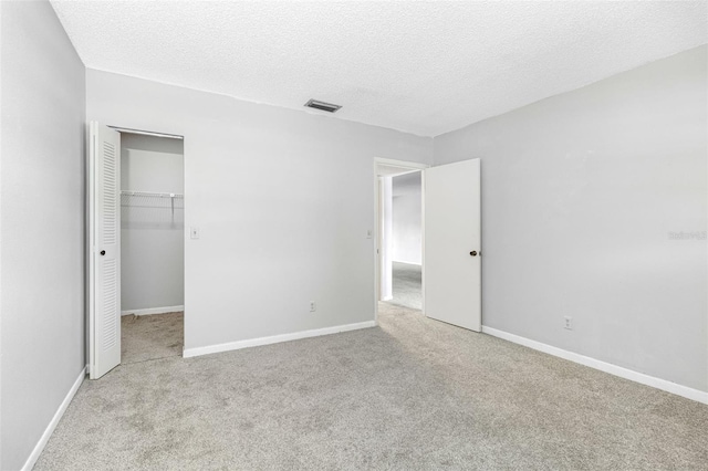 unfurnished bedroom featuring a walk in closet, light carpet, a textured ceiling, and a closet