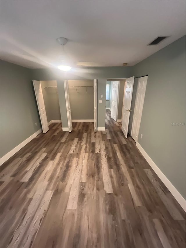 unfurnished bedroom with dark hardwood / wood-style floors and two closets