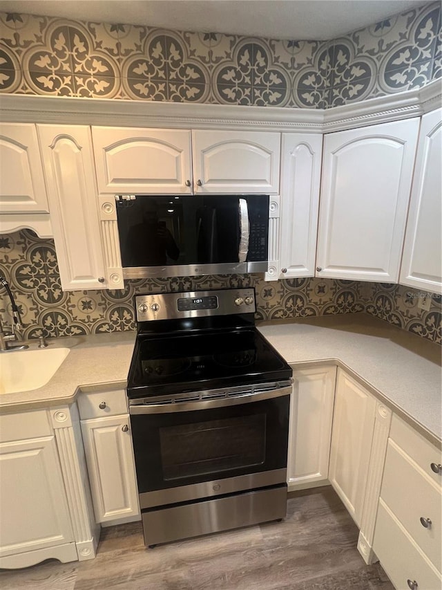 kitchen featuring hardwood / wood-style flooring, appliances with stainless steel finishes, sink, and white cabinets