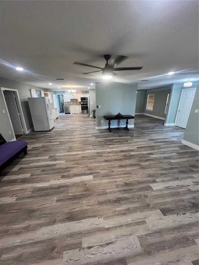 unfurnished living room featuring dark wood-type flooring, ceiling fan, and a textured ceiling