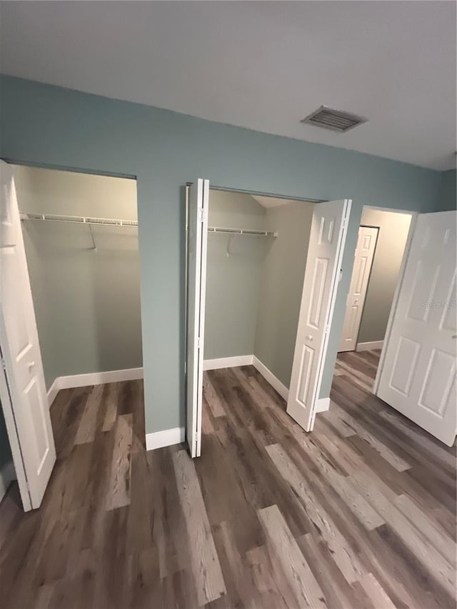 unfurnished bedroom with multiple closets and dark wood-type flooring