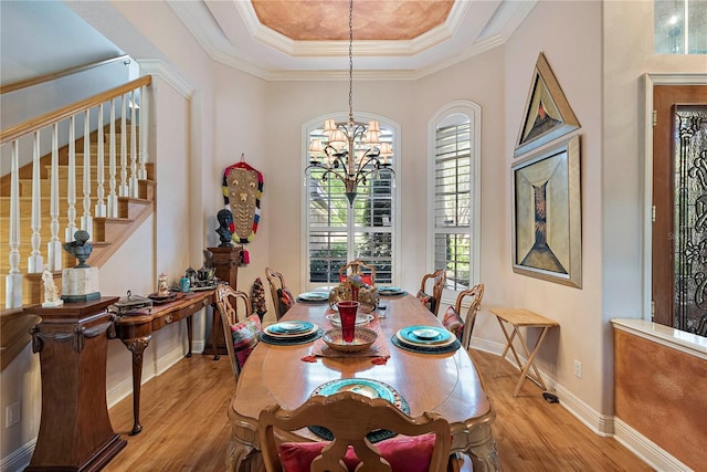 dining room with a notable chandelier, crown molding, a raised ceiling, and light wood-type flooring