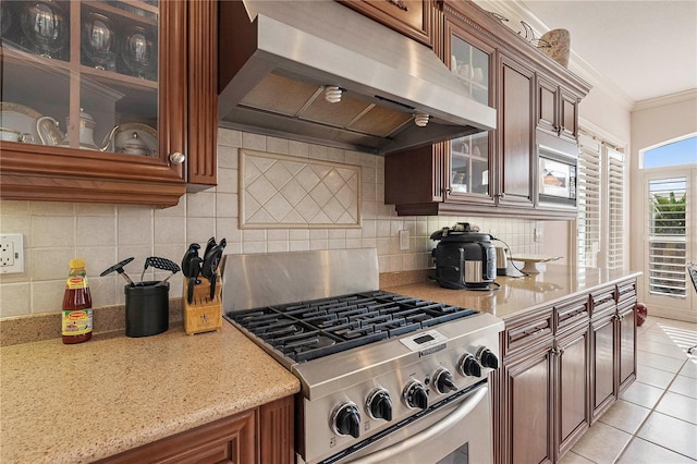 kitchen with range hood, backsplash, ornamental molding, light tile patterned floors, and gas range