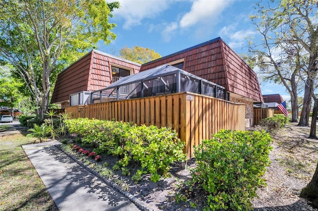 view of home's exterior with brick siding, glass enclosure, and mansard roof