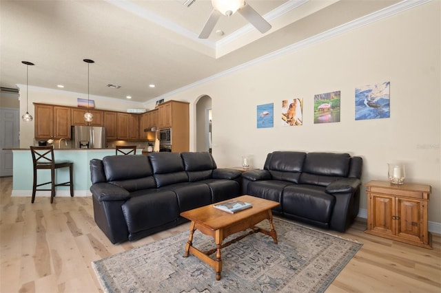 living room with sink, light hardwood / wood-style flooring, ornamental molding, a raised ceiling, and ceiling fan