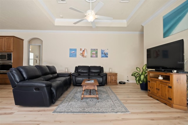 living room with ceiling fan, ornamental molding, a raised ceiling, and light wood-type flooring