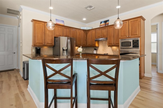 kitchen featuring dark stone counters, a kitchen breakfast bar, an island with sink, pendant lighting, and stainless steel appliances