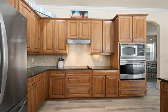 kitchen featuring appliances with stainless steel finishes, light hardwood / wood-style floors, ornamental molding, decorative backsplash, and dark stone counters