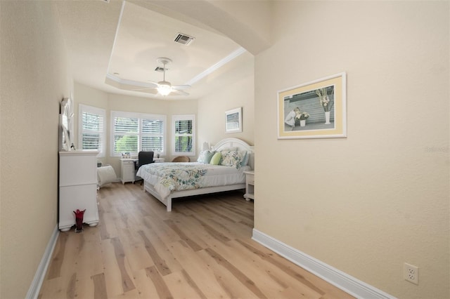 bedroom with a tray ceiling, ornamental molding, light hardwood / wood-style floors, and ceiling fan