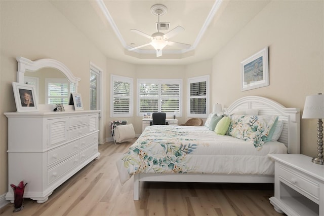 bedroom featuring ceiling fan, ornamental molding, a tray ceiling, and light hardwood / wood-style flooring