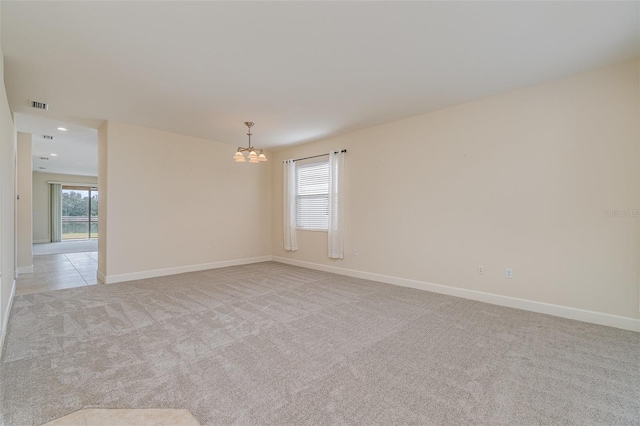 empty room with light colored carpet, a notable chandelier, and a wealth of natural light