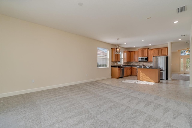 kitchen with appliances with stainless steel finishes, decorative backsplash, a kitchen island, decorative light fixtures, and light colored carpet