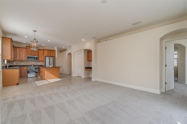 kitchen featuring pendant lighting, a kitchen island, light colored carpet, and appliances with stainless steel finishes