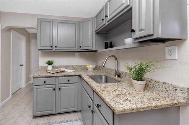 kitchen with gray cabinetry, sink, light tile patterned floors, and light stone counters