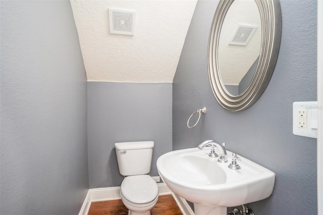 half bath featuring wood finished floors, visible vents, baseboards, a sink, and toilet