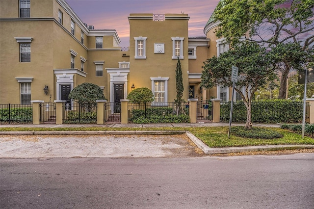 townhome / multi-family property with a gate, uncovered parking, a fenced front yard, and stucco siding