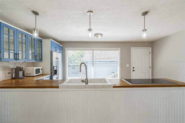 kitchen featuring blue cabinets, sink, stainless steel fridge, pendant lighting, and black electric stovetop