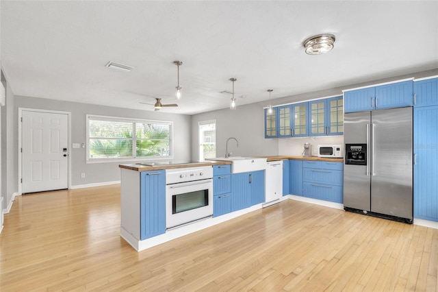 kitchen featuring blue cabinets, decorative light fixtures, light hardwood / wood-style flooring, kitchen peninsula, and white appliances