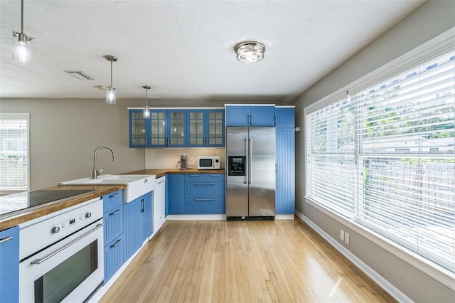 kitchen with blue cabinets, sink, light wood-type flooring, pendant lighting, and white appliances