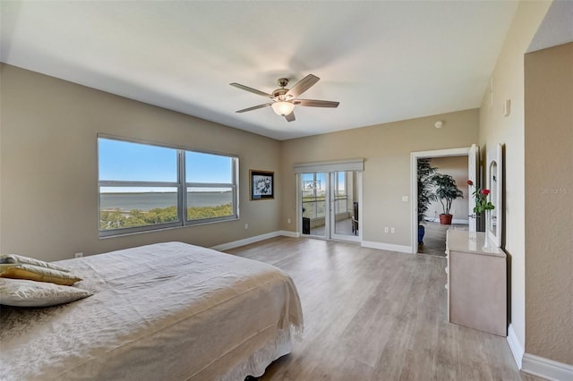 bedroom with a walk in closet, access to exterior, ceiling fan, a water view, and light hardwood / wood-style flooring