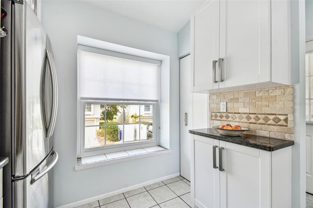 kitchen featuring white cabinetry, dark stone counters, stainless steel refrigerator, and decorative backsplash