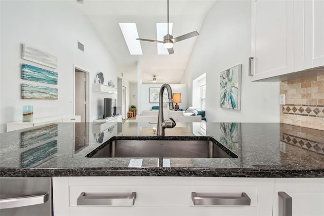 kitchen with white cabinetry, sink, vaulted ceiling with skylight, and dark stone counters